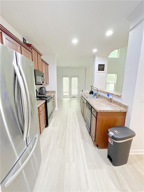 3130 Haynes Park Dr, Lithonia, GA 30038 - kitchen featuring stainless steel appliances, a sink, brown cabinetry, baseboards, and light wood-type flooring