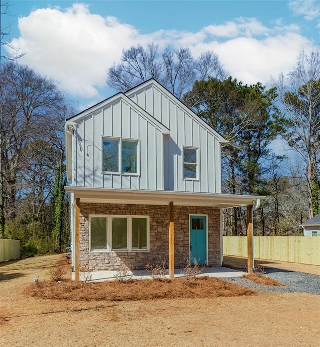 view of front of property with board and batten siding, stone siding, and fence