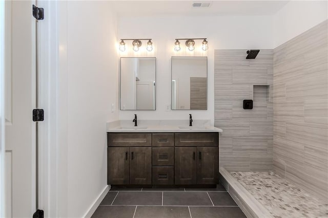 bathroom with double vanity, tiled shower, a sink, and tile patterned floors