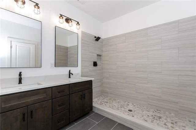 full bath with double vanity, tiled shower, tile patterned flooring, and a sink