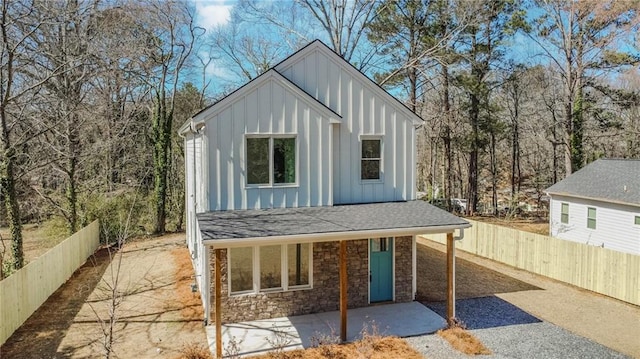 exterior space featuring fence private yard, a shingled roof, stone siding, board and batten siding, and a patio area