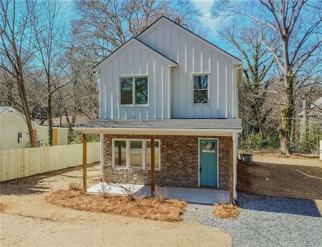 view of front of house with stone siding, fence, covered porch, and board and batten siding