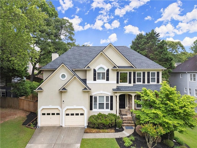 traditional-style house featuring stucco siding, fence, an attached garage, driveway, and a chimney