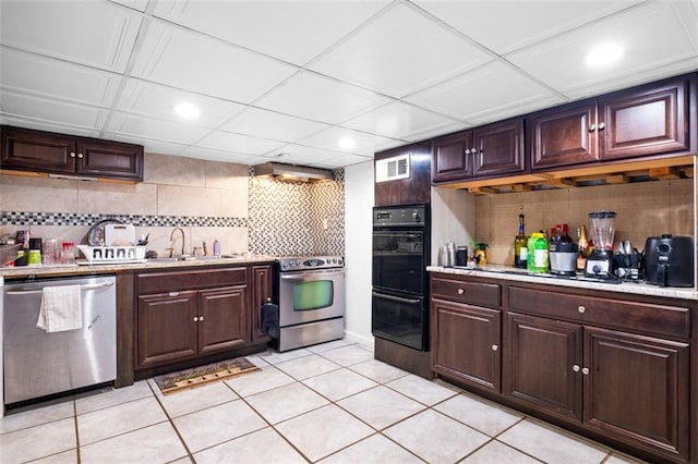 kitchen featuring dark brown cabinetry, sink, stainless steel appliances, backsplash, and light tile patterned floors