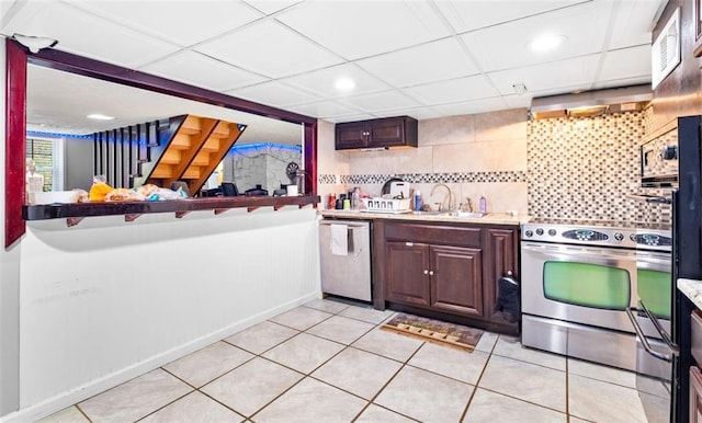 kitchen with a paneled ceiling, wall chimney range hood, stainless steel appliances, and light tile patterned floors