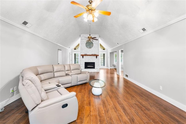 living room with vaulted ceiling, hardwood / wood-style flooring, a stone fireplace, and crown molding