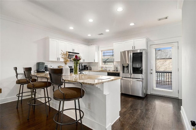 kitchen with a breakfast bar, stainless steel refrigerator, backsplash, white cabinets, and light stone countertops