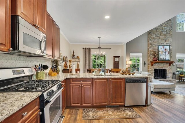 kitchen with stainless steel appliances, a sink, a peninsula, a chandelier, and light wood-style flooring