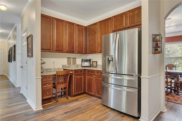 kitchen with stainless steel refrigerator with ice dispenser, light wood finished floors, arched walkways, ornamental molding, and light stone counters