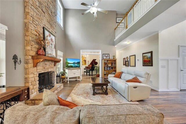 living area featuring a towering ceiling, wood finished floors, a fireplace, baseboards, and ornamental molding