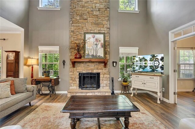 living room with a towering ceiling, a stone fireplace, wood finished floors, baseboards, and ornamental molding