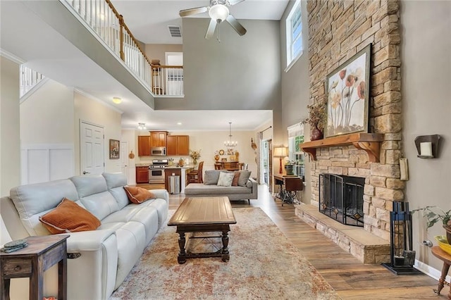 living room with a high ceiling, light wood-style floors, ceiling fan, a stone fireplace, and a chandelier