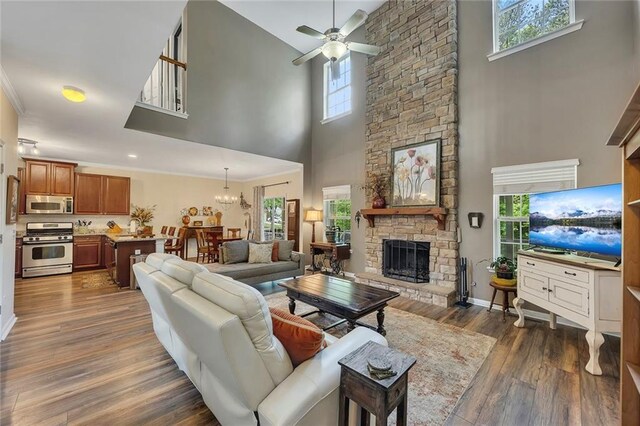 living area with a towering ceiling, ceiling fan, a fireplace, dark wood-style floors, and a chandelier