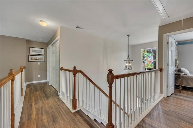 corridor with an upstairs landing, attic access, and wood finished floors