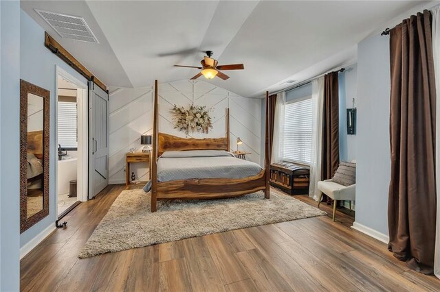 bedroom with a barn door, wood finished floors, lofted ceiling, a ceiling fan, and baseboards