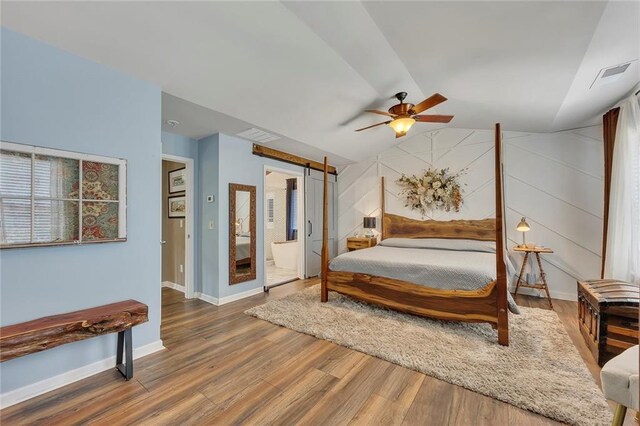 bedroom with a barn door, wood finished floors, vaulted ceiling, ceiling fan, and baseboards