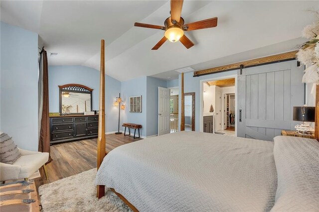 bedroom featuring wood finished floors, lofted ceiling, a barn door, ceiling fan, and baseboards