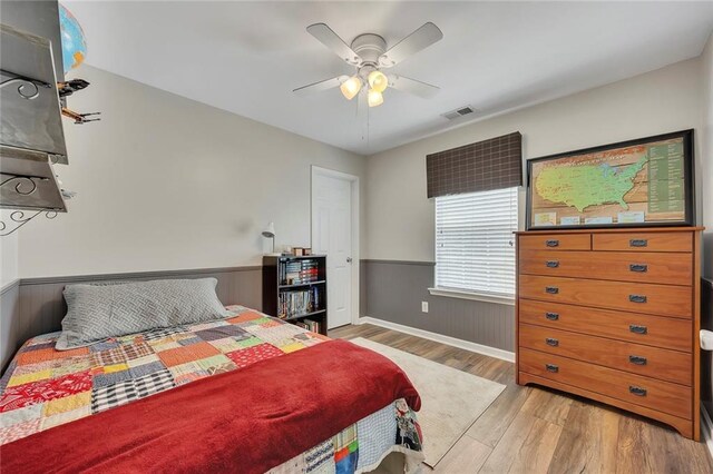 bedroom with wood finished floors, a ceiling fan, baseboards, and wainscoting