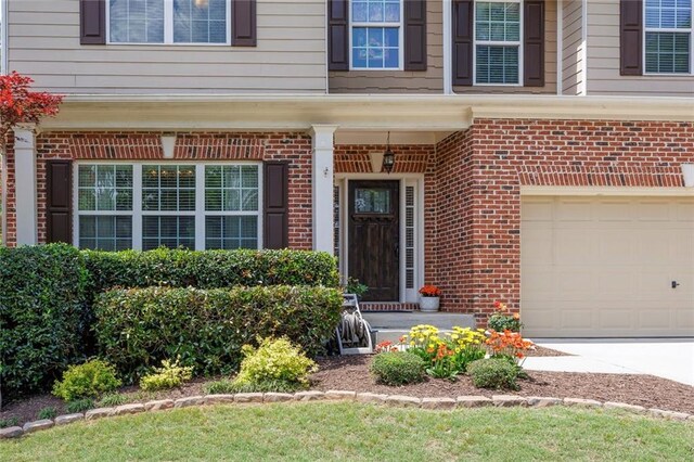 doorway to property with brick siding, an attached garage, and driveway