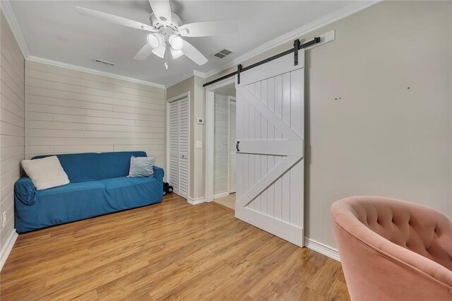sitting room with a barn door, ceiling fan, light wood-style floors, ornamental molding, and baseboards