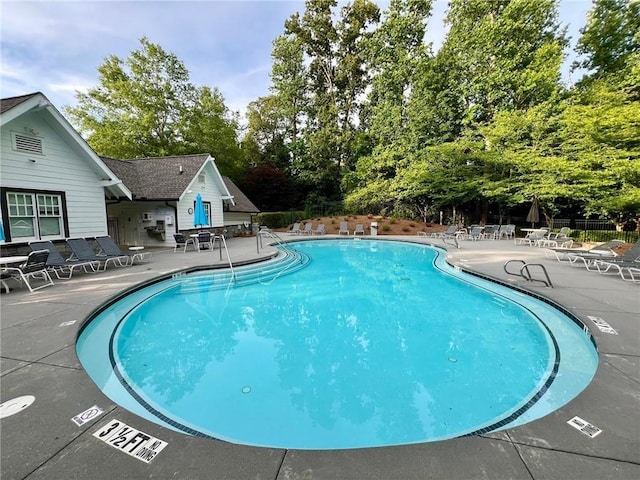 community pool featuring a patio area, view of wooded area, and fence