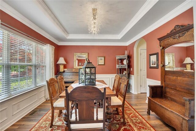 dining area with a raised ceiling, arched walkways, wood finished floors, a chandelier, and wainscoting