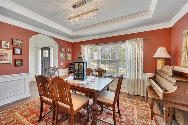dining area featuring a tray ceiling, arched walkways, a wainscoted wall, ornamental molding, and wood finished floors