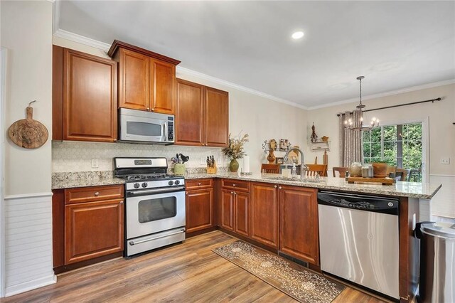 kitchen featuring stainless steel appliances, a sink, a peninsula, a chandelier, and crown molding