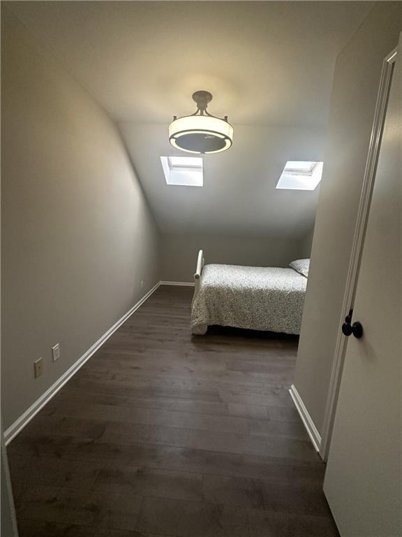 unfurnished bedroom featuring vaulted ceiling with skylight, baseboards, and dark wood-style flooring