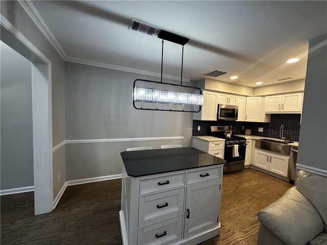 kitchen featuring stainless steel appliances, dark countertops, hanging light fixtures, white cabinetry, and a sink