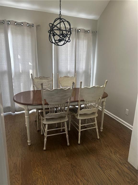 dining space with an inviting chandelier, baseboards, and dark wood-type flooring