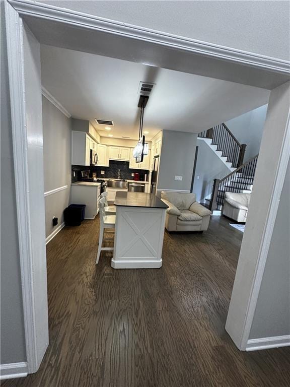 kitchen featuring dark countertops, a kitchen breakfast bar, dark wood-type flooring, decorative light fixtures, and white cabinetry