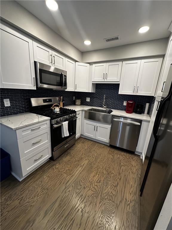 kitchen featuring stainless steel appliances, white cabinetry, a sink, and visible vents