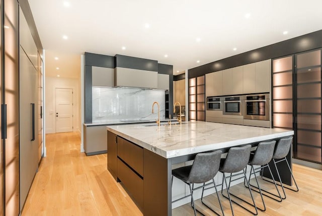 kitchen with a spacious island, stainless steel oven, light stone countertops, and gray cabinetry