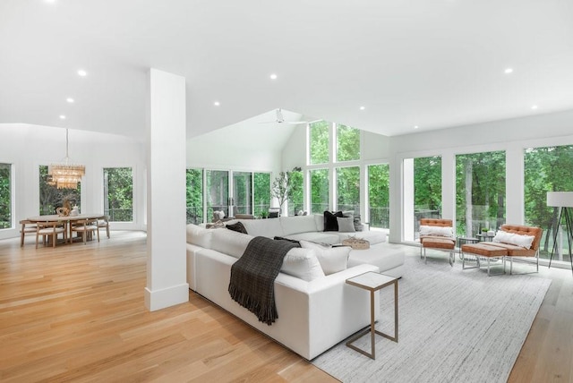 living room featuring an inviting chandelier, a wealth of natural light, high vaulted ceiling, and light wood-type flooring