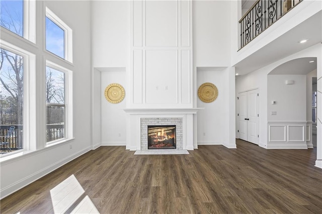 unfurnished living room featuring a high ceiling, a brick fireplace, and dark hardwood / wood-style floors