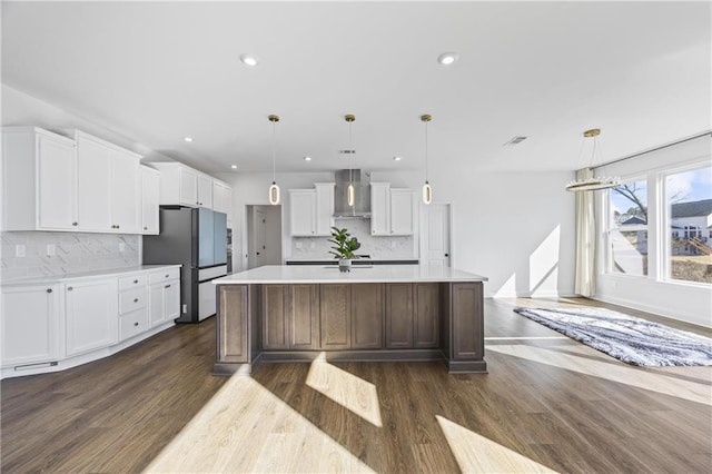 kitchen featuring pendant lighting, stainless steel fridge, white cabinets, a large island with sink, and wall chimney range hood