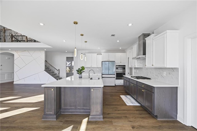 kitchen featuring appliances with stainless steel finishes, pendant lighting, white cabinets, wall chimney range hood, and a spacious island