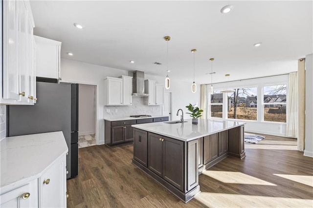 kitchen with wall chimney exhaust hood, sink, hanging light fixtures, a kitchen island with sink, and backsplash