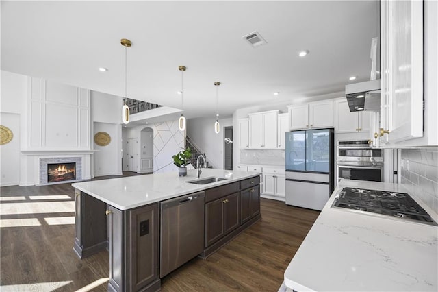 kitchen featuring white cabinetry, a large island with sink, appliances with stainless steel finishes, pendant lighting, and a fireplace