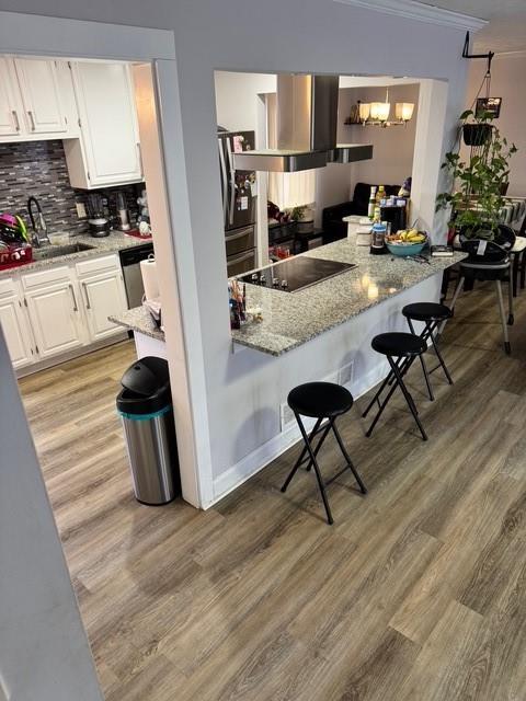 kitchen featuring a breakfast bar area, stainless steel appliances, light stone countertops, white cabinets, and light wood-type flooring