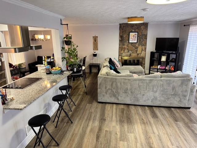 living room with crown molding, hardwood / wood-style floors, a stone fireplace, and a textured ceiling