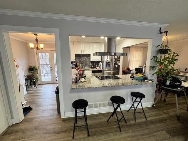 kitchen with white cabinetry, stainless steel appliances, a breakfast bar area, and wall chimney range hood