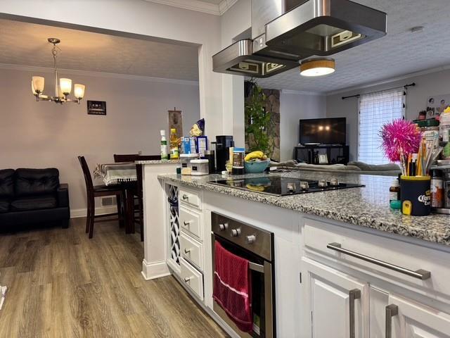 kitchen with decorative light fixtures, white cabinetry, black electric stovetop, stainless steel oven, and crown molding