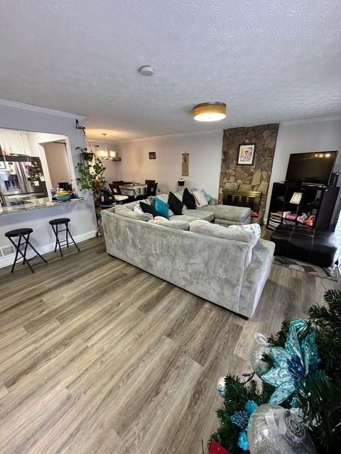 living room featuring hardwood / wood-style floors, a notable chandelier, a fireplace, ornamental molding, and a textured ceiling