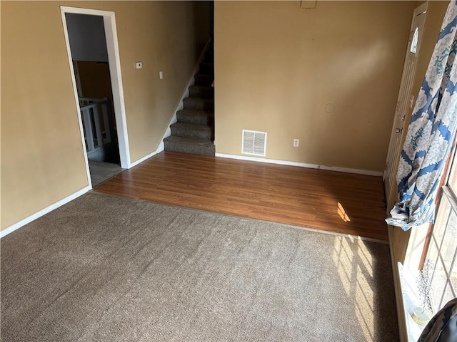 unfurnished living room with visible vents, wood finished floors, carpet, baseboards, and stairs