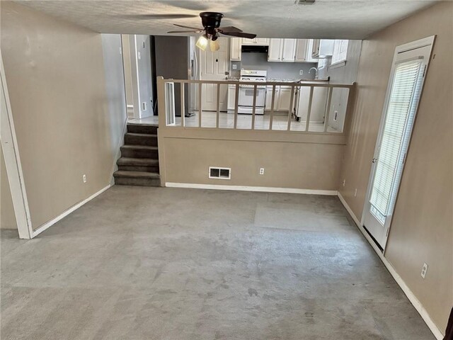 unfurnished living room featuring carpet floors, ceiling fan, a fireplace, and a textured ceiling