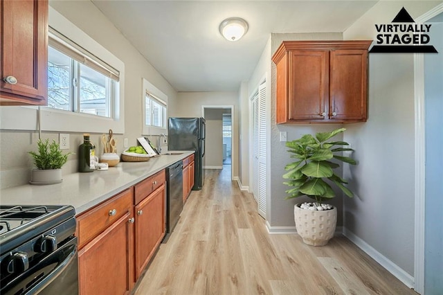 kitchen featuring light wood finished floors, baseboards, light countertops, black appliances, and a sink