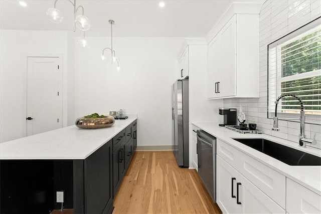 kitchen featuring sink, appliances with stainless steel finishes, decorative light fixtures, light hardwood / wood-style floors, and white cabinetry