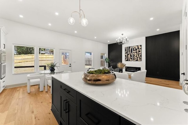 kitchen featuring pendant lighting, light stone counters, light wood-type flooring, and an inviting chandelier